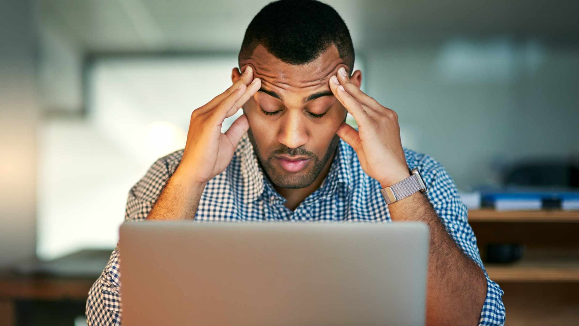 man with hands on head stressed out and deeply worried sitting at his laptop