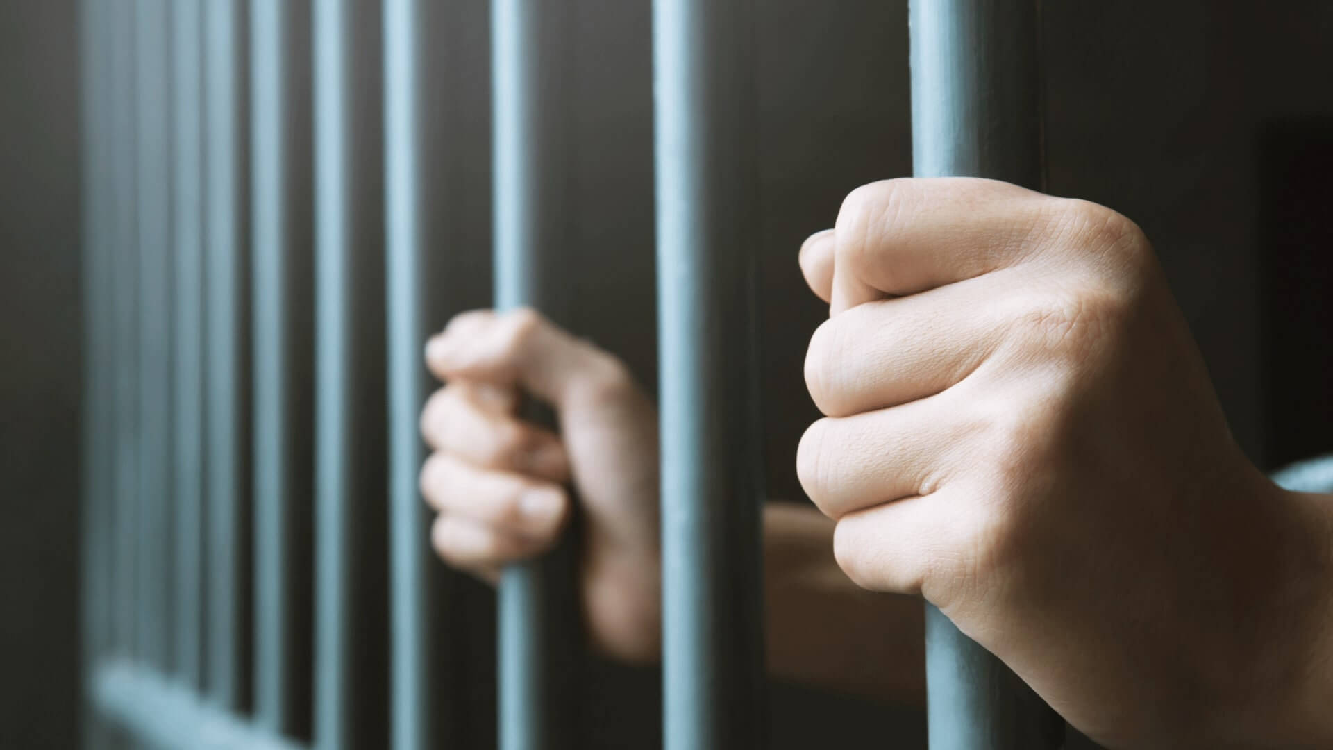 person locked up in jail holding onto jailbars
